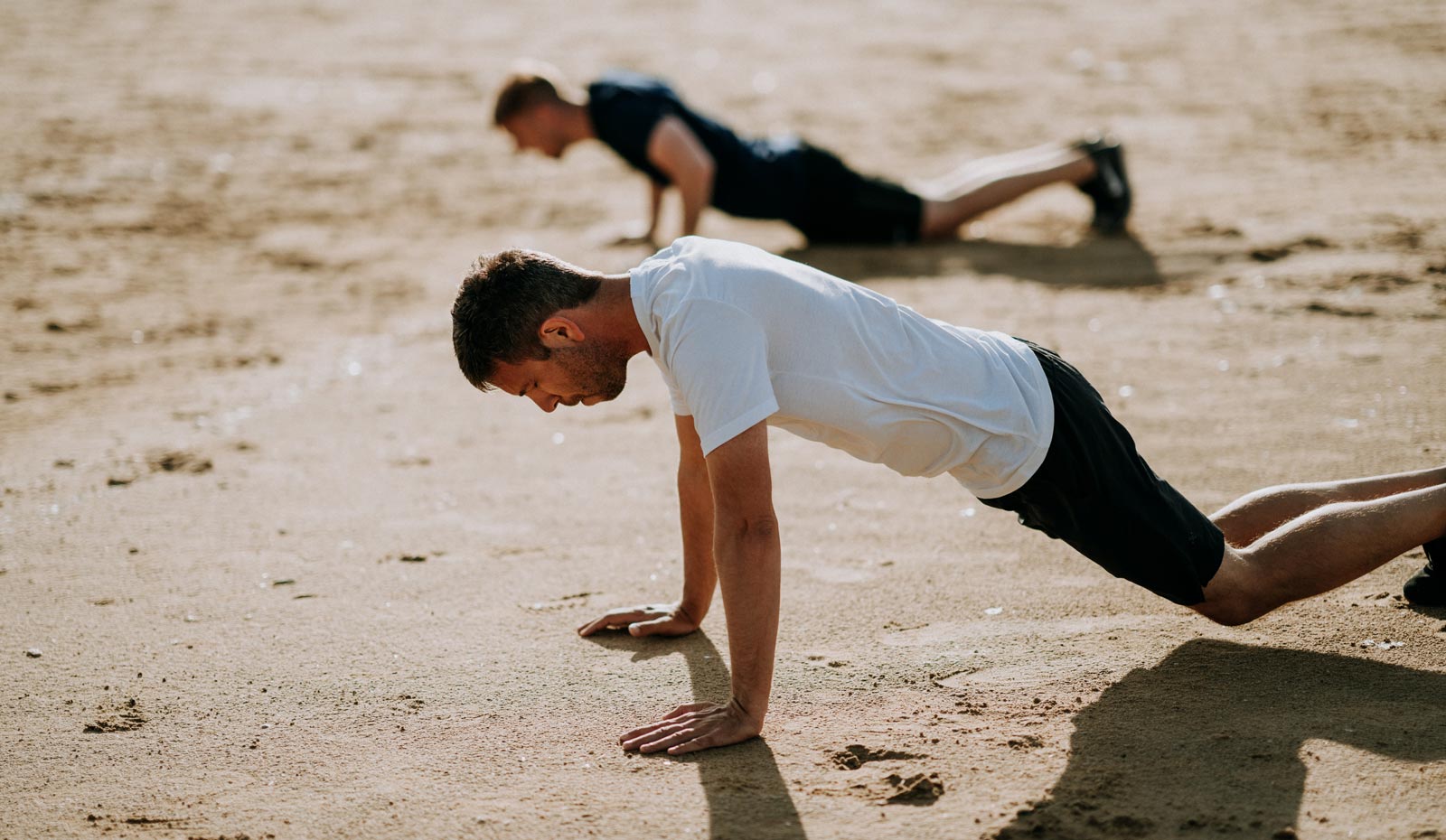 Two guys doing push ups on sandy beach